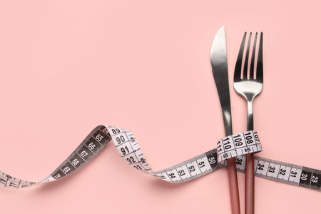 New measuring tape with cutlery on pink background, closeup