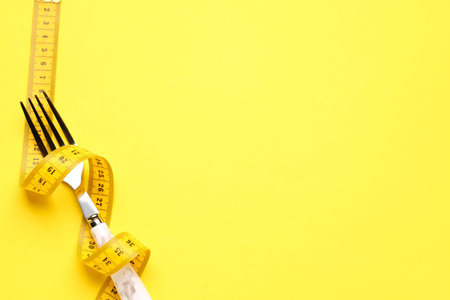 New measuring tape and fork on yellow background, closeupの写真素材