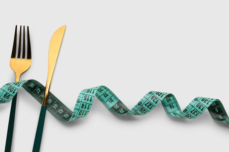 New measuring tape and cutlery on light background, closeup
