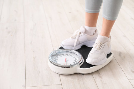 Young woman measuring her weight on scales at home, closeupの写真素材