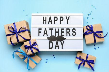 Board with text HAPPY FATHER'S DAY and gift boxes on color backgroundの写真素材