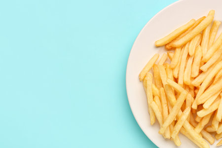 Plate with tasty french fries on light blue background