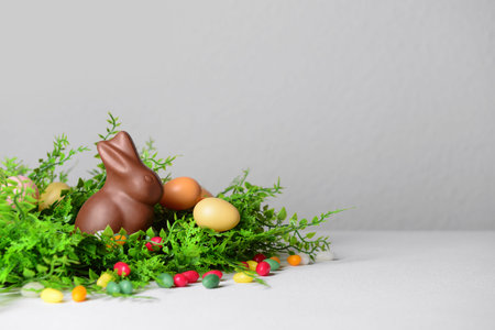 Chocolate bunny, Easter eggs and candies in plant leaves on white table