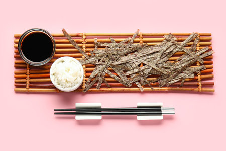 Bamboo mat with cut nori sheets, rice, soy sauce and chopsticks on pink backgroundの写真素材