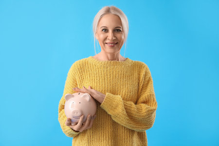 Mature woman with piggy bank on blue backgroundの写真素材