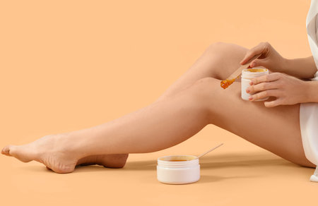 Young woman applying sugaring paste onto her legs against beige backgroundの写真素材