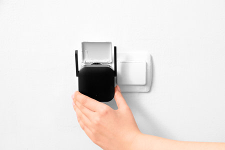 Woman plugging black WiFi repeater in electric socket on white wallの写真素材