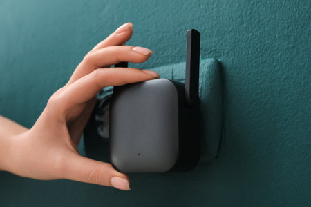 Woman plugging black WiFi repeater in electric socket on green wallの写真素材