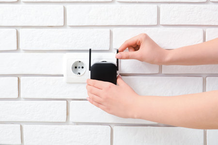 Woman plugging black WiFi repeater in electric socket on white brick wallの写真素材