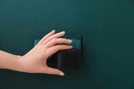 Woman plugging black WiFi repeater in electric socket on green wallの写真素材