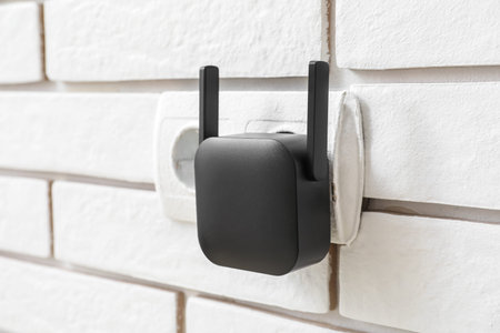 Black WiFi repeater in electric socket on white brick wall