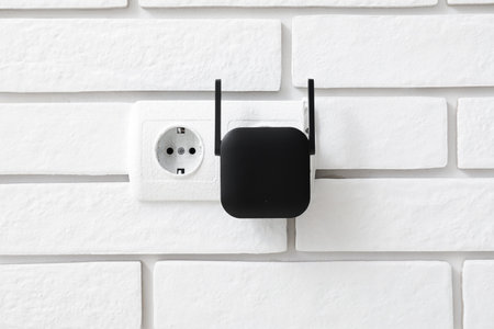 Black WiFi repeater in electric socket on white brick wallの写真素材