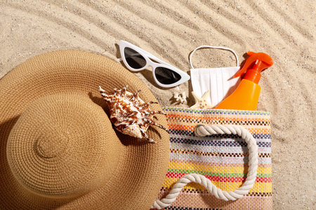 Bag with bottle of sunscreen cream, medical mask, beach accessories and seashells on sand. melanoma...