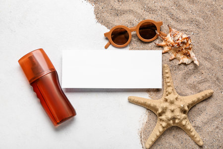 Composition with blank card, bottle of sunscreen cream, sunglasses and sand on light backgroundの写真素材
