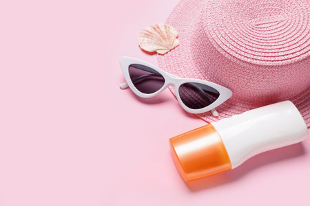 Bottle of sunscreen cream, hat, sunglasses and seashell on pink background. melanoma concept