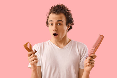 Shocked young man with hair loss problem and combs on pink backgroundの写真素材