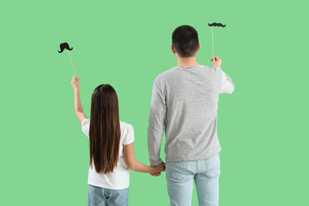 Father and his little daughter with paper mustache on green background, back viewの写真素材