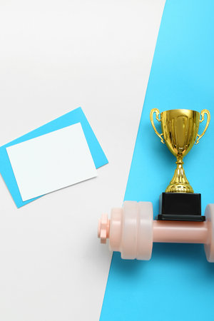 Blank card with gold cup and dumbbell on color backgroundの写真素材