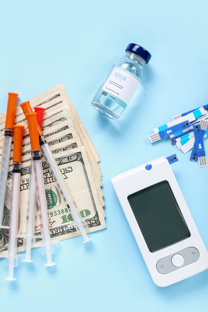Insulin with glucometer, lancet pens, syringes and money on blue background. Expensive medicine conceptの写真素材