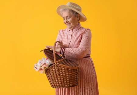 Senior woman with basket of flowers on yellow backgroundの写真素材