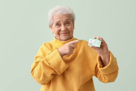 Senior woman pointing at driving license on green backgroundの写真素材