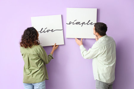 Young couple hanging posters on lilac wallの写真素材