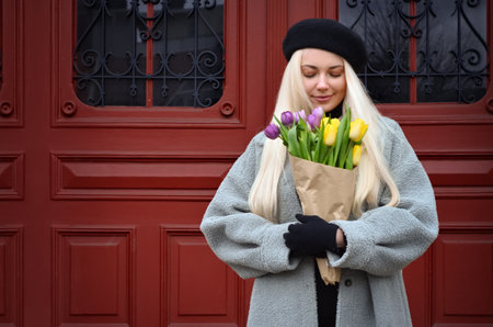 Young woman with bouquet of tulips near door on city streetの写真素材