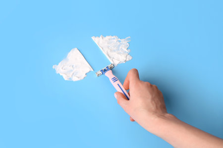 Female hand with safety razor and shaving foam on color backgroundの写真素材