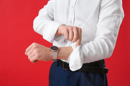 Young businessman rolling up his sleeve on red background, closeup