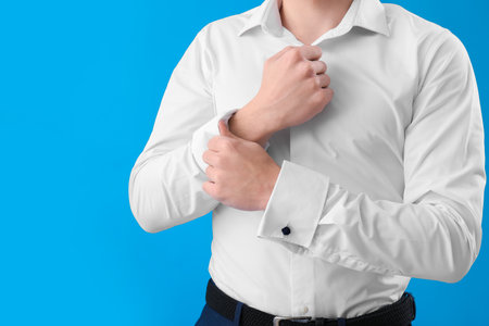 Young businessman rolling up his sleeve on light blue background, closeupの写真素材