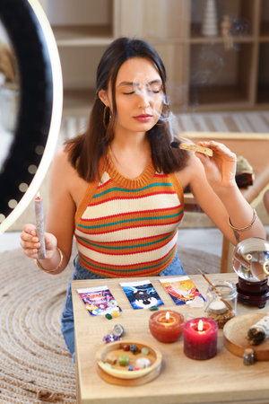 Young witch cleansing space with palo santo while recording video for blog at home