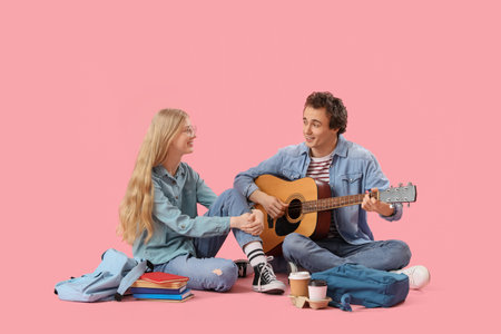 Teenage girl with her boyfriend playing guitar on pink backgroundの写真素材
