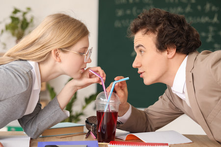 Teenage couple drinking juice with straws in classroomの写真素材