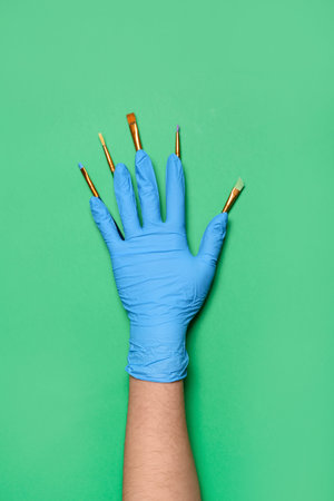 Makeup artist in rubber glove with brushes on green background