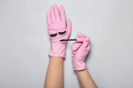 Makeup artist in pink gloves with mascara and fake eyelashes on gray backgroundの写真素材