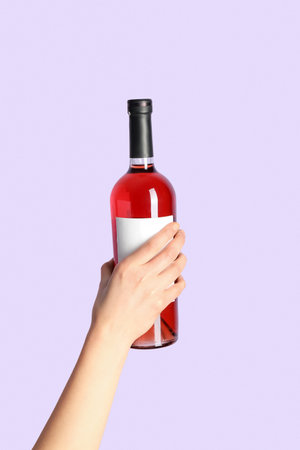 Female hand holding bottle of red wine on lilac backgroundの写真素材