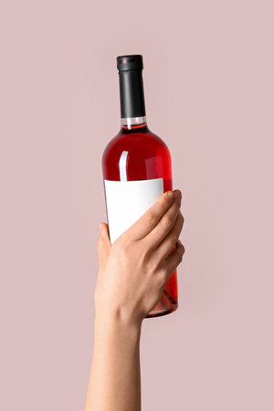 Female hand holding bottle of red wine on pink backgroundの写真素材