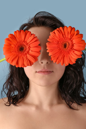 Young woman closing eyes with beautiful gerbera flowers on blue backgroundの写真素材