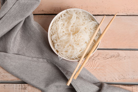Bowl with tasty rice noodles and chopsticks on light wooden tableの写真素材