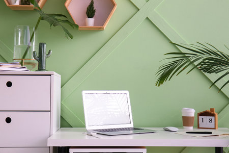 Workplace with laptop and cup of coffee near green wall in officeの写真素材