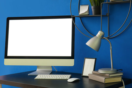 Workplace with computer, books and lamp near blue wall in office
