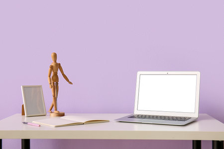 Workplace with laptop, mannequin and frame near lilac wallの写真素材