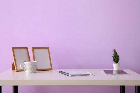 Workplace with tablet computer, notebook and blank frames near lilac wallの写真素材