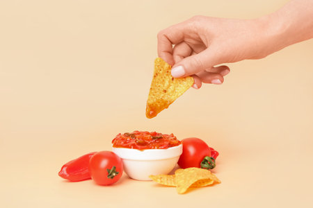 Woman dipping nacho into tasty salsa sauce on color backgroundの写真素材