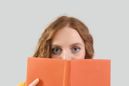 Beautiful redhead woman with book on gray background, closeupの写真素材