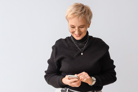 Beautiful mature woman using mobile phone on light backgroundの写真素材