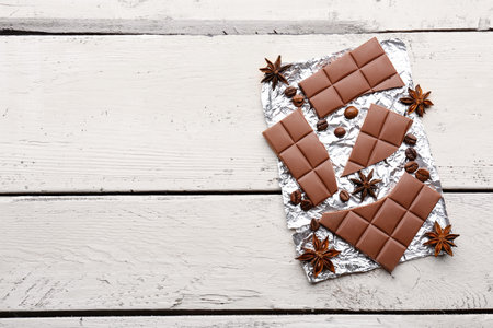 Foil with tasty chocolate, coffee beans and anise stars on light wooden backgroundの写真素材