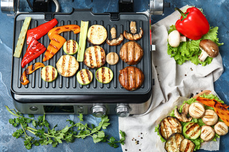 Modern electric grill with tasty vegetables on blue backgroundの写真素材