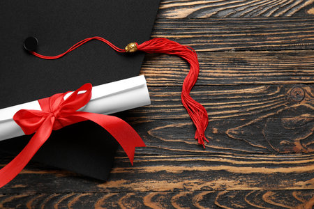 Diploma with red ribbon and graduation hat on wooden tableの写真素材