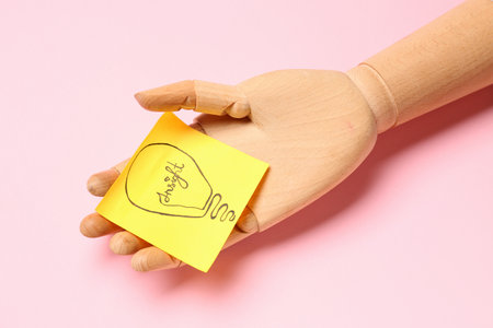 Wooden hand and sticky paper with drawn light bulb on pink backgroundの写真素材